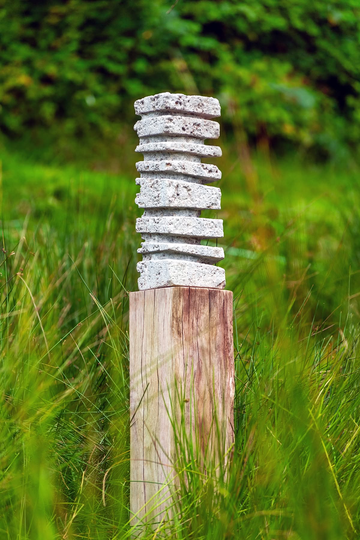 Gestapelte Steinskulptur auf einem Holzpfahl in einer Sommerwiese am Gesäßhof