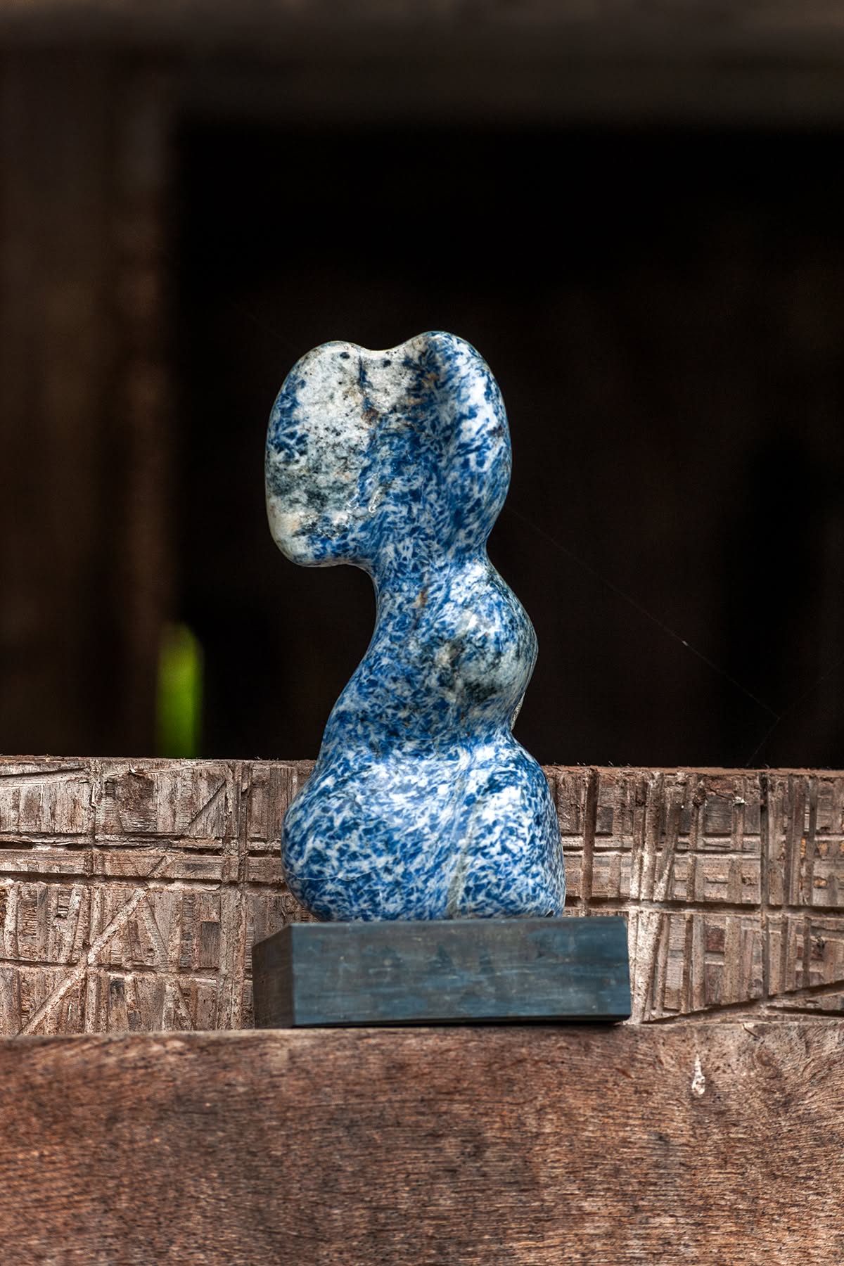 Blau-weiß gemaserte Steinskulptur auf einem Holzbalken am Gesäßhof